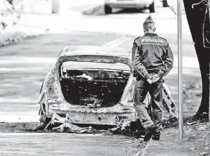  ?? Marcelo Gonçalves/Sigmapress ?? Policial militar observa carro queimado encontrado na rua Leonor Quadros, no Morumbi (zona oeste de SP); no porta-malas do veículo havia um corpo carbonizad­o; caso semelhante ocorreu a 850 metros de lá