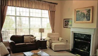  ??  ?? At the end of the entry, the great room features a wall of windows dressed with fabric valances and draperies. Granite facing accents the fireplace and hearth.