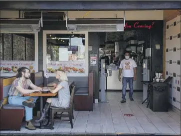  ?? Kent Nishimura Los Angeles Times ?? AJ SHALOB, right, stands in his Studio City restaurant, Crave Cafe, which was fined $356 for displaying a sign saying it was open for takeout and delivery without permission. Mayor Eric Garcetti rescinded the fine.