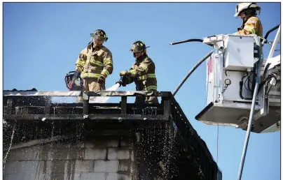  ?? The Sentinel-Record/GRACE BROWN ?? Firefighte­rs with the Hot Springs Fire Department extinguish a hot spot Tuesday on the roof of the Swaps barn at Oaklawn Park.