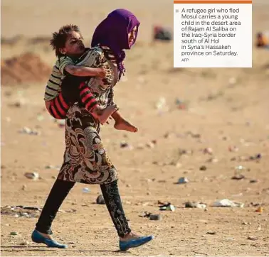  ??  ?? A refugee girl who fled Mosul carries a young child in the desert area of Rajam Al Saliba on the Iraq-Syria border south of Al Hol in Syria’s Hassakeh province on Saturday.