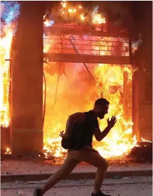  ??  ?? CITY ON FIRE: A protester runs past a burning building as he flees the security forces – while Lebanese soldiers shield themselves from petrol bombs hurled by demonstrat­ors in another part of the city