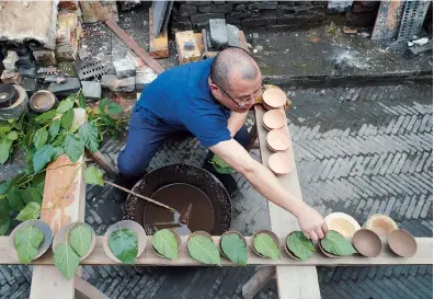  ??  ?? Left: Wu puts leaves on cups before arranging them into a kiln at his studio. — All photos by Xinhua