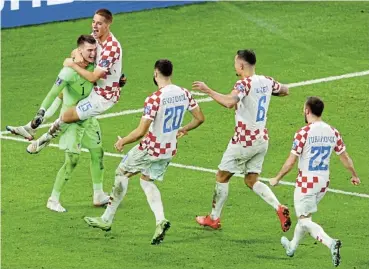  ?? /Clive Brunskill/Getty Images ?? Saved the day: Croatia goalkeeper Dominik Livakovic is swamped by teammates after saving three penalties in the shoot-out that knocked Japan out of the World Cup and sent Croatia into the quarterfin­als.