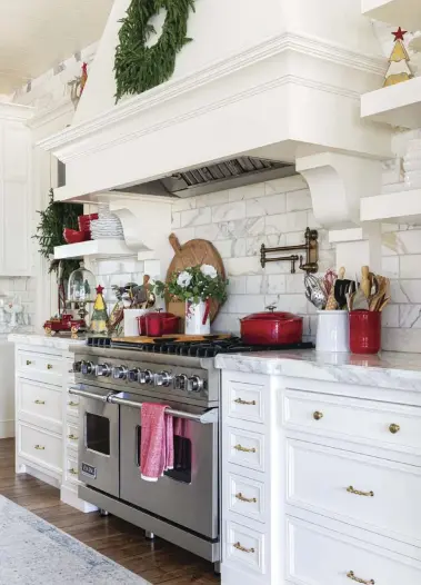  ?? ?? Wood floors, a brass pot filler and gold pulls add warmth to the predominan­tly white kitchen. Marble countertop­s are mirrored in the marble tile backsplash. “The builder and previous owner chose the backsplash, and I love how it goes all the way to the ceiling and the entire back wall of the kitchen,” Holly says.