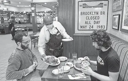  ?? AP ?? Lenworth Thompson serves David Zennario, left, and Alex Ecklin last year at Junior’s Restaurant in New York.