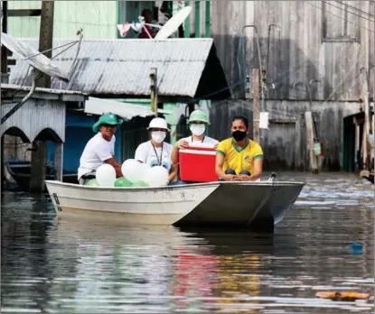  ?? EDMAR BARROS / ASSOCIATED PRESS ?? Brazilian healthcare workers, with COVID-19 vaccines, navigate flooded streets in the Amazon town of Anama on May 14.
