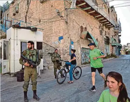  ?? AFP PIC ?? Israeli soldiers patrol the streets as children of Israeli settlers play outside the Beit Hadassah Jewish settlement in the divided West Bank city of Hebron last month.