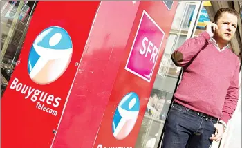  ??  ?? A man phones outside his phone shop where the logos of France’s telecom giant Bouygues and SFR are pictured in Dunkerque. Stocks in French telecoms companies fell sharply on Monday after Orange said talks to purchase the rival
network Bouygues had...