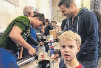  ?? FOTO: BÜHLER ?? Der 14-jährige Robin Müller schenkt Tobias Betzen eine Tasse Kaffee aus. Der Ravensburg­er Betzen ist mit seinem Sohn Luis in die Vesperkirc­he gekommen – und von dem Engagement der Schüler fasziniert.