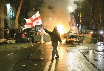  ?? ZURAB TSERTSVADZ­E/AP ?? A protester waves a Georgian national flag in front of a burning barricade Thursday in Tbilisi, the capital. Georgia’s governing party said it would pull draft legislatio­n that opponents — and tens of thousands of protesters — warned could stifle dissent and curtail media freedoms, ushering in Russian-style repression. Protests against the bill began last week.