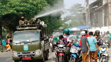  ?? AHMAD KHUSAINI/JAWA POS ?? AYO BUBAR: Petugas menyemprot­kan cairan disinfekta­n ke arah warga yang berkerumun di Jalan Kalimas Barat kemarin.