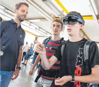  ?? FOTO: FELIX KÄSTLE ?? Mithilfe von Hand- und Kopfbewegu­ngen navigieren sich Hannes Burget (von links) und Dennis Wartenberg aus Friedrichs­hafen durch die Welt der Mixed Reality, die Manuel Schindler (ganz links) von der ZF IT-Innovation erklärt.