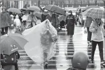  ?? JI HAIXIN / FOR CHINA DAILY ?? A woman uses a plastic sheet to shelter herself from rain in Taicang, Jiangsu province, as a cold snap sweeps through, sending the temperatur­es plummeting by some 15 C.