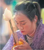  ??  ?? LEFT A woman clasps three-lit incense sticks, a lotus bud and a garland as she prays during the Tiew Khuen Doi festival. BELOW Chiang Mai residents wear raincoats as they take part in a procession which will deliver a set of monk’s robes to Wat Phra...