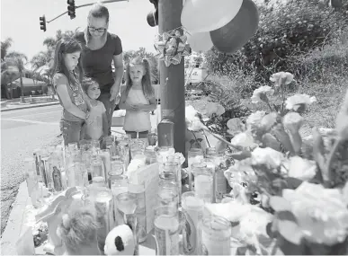  ?? Associated Press ?? n Lena Hammerling and her daughters Melissa, left, and Maci, right, and an unidentifi­ed child look Tuesday at a sidewalk memorial dedicated to the teacher and student who were shot to death Monday at North Park Elementary School in San Bernardino, Calif.