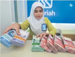  ?? AFP ?? An employee of BRI Syariah Bank handles bundles of Indonesian rupiah banknotes in Jakarta.