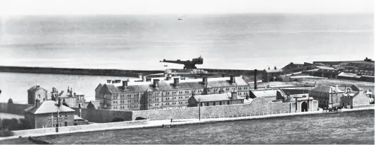  ??  ?? A commercial postcard of Peterhead convict prison – perhaps not a case of ‘Wish you were here’ – with the 160ft end-to-end length of the Titan crane on the South Breakwater seen the background, and the site of the barge harbour evident between the crane and the prison. The sheds forming the workshop and Admiralty station area are to the far right. Built in 1888 and initially intended to house 208 prisoners, the evolved prison later held well over 400, while in 2012, with hard labour long since a thing of the past, Peterhead prison could officially accommodat­e 142 prisoners. It closed the following year, the former works yard having been adopted as the site for Her Majesty’s Prison Grampian, a new facility with a capacity of about 500, including men and women, and young offenders. The old prison is now a museum. Author’s Collection