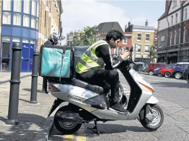  ?? REUTERS ?? This file photo shows a Deliveroo scooter driver taking a break between deliveries in London.