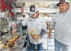  ?? Marvin Pfeiffer / Staff photograph­er ?? Champion barbecue cook Corey Flores (right) watches teammate Richie Cunningham apply a glaze to a rack ribs in their trailer.