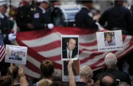  ?? BRENDAN SMIALOWSKI/AFP/GETTY IMAGES ?? Family and friends hold photos of victims during a service at the 9/11 memorial Sunday. Relatives of the dead reflected on how the attacks affected them.
