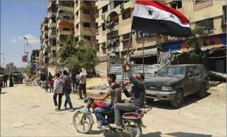  ?? SANA VIA AP ?? Syrian men riding a motorcycle wave their national flag, after Syrian police units entered the town of Douma, the site of a suspected chemical weapons attack and the last rebel-held town in the eastern Ghouta, near Damascus, Syria. Syrian state TV is...