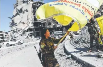  ?? Bulent Kilic, AFP/Getty Images ?? Rojda Felat, a Syrian Democratic Forces commander, waves her group’s flag at iconic Naim, or Paradise Square, in Raqqa on Tuesday. U.S.-backed forces said they had taken full control of Raqqa from the Islamic State terrorist group.