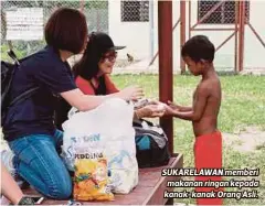  ??  ?? SUKARELAWA­N memberi makanan ringan kepada kanak-kanak Orang Asli.