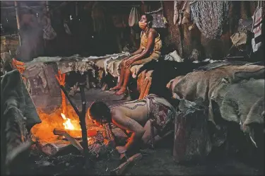  ??  ?? Tatanka Gibson (kneeling) a member of the Haliwa band of Nansemond and Saponi and a museum educator at Plimoth Plantation, a reconstruc­ted living history exhibit, starts a fire inside a nush wetu after getting soaked in a downpour while waiting for visitors at the Wampanoag Homesite in Plymouth, Mass.
(AP/David Goldman)