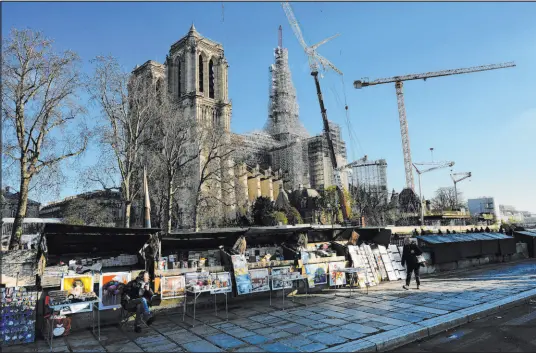  ?? Thibault Camus The Associated Press ?? Book sellers wait in front of Notre Dame cathedral in Paris, with its spire surrounded by scaffoldin­g Wednesday.