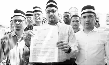  ??  ?? Shaiful (centre) shows the police report lodged against a social media user who allegedly posted insulting comments on the demise of Sultan Abdul Halim at the Kota Setar police headquarte­rs. — Bernama photo