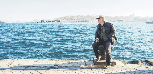  ?? ?? A man sits on a bollard in the Karaköy district with Topkapı Palace and Hagia Sophia Grand Mosque (R) in the background, Istanbul, Türkiye, Feb. 22, 2024.