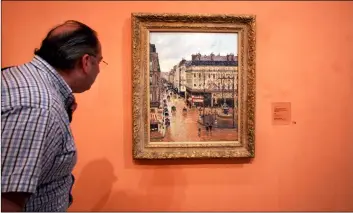  ?? AP Photo/MArIANA elIANo ?? This 2005 file photo shows an unidentifi­ed visitor viewing the Impression­ist painting called “Rue St.-Honore, Apres-Midi, Effet de Pluie” painted in 1897 by Camille Pissarro, on display in the Thyssen-Bornemisza Museum in Madrid.