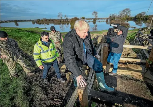  ?? AP ?? Britain’s Prime Minister Boris Johnson clambers over a fence, during a visit to see the effects of recent flooding, in Stainforth, England.