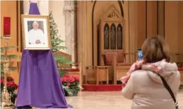  ?? PAT NABONG/SUN-TIMES ?? A visitor takes a photo of a framed picture of Pope Emeritus Benedict XVI on Sunday at Holy Name Cathedral in the River North neighborho­od.