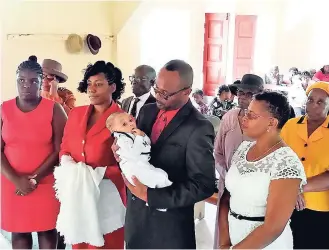  ?? GEORGE HENRY ?? Father Royston Hinds looks closely at his son, Cayleb, while mother Anna-Kay McDonald (second right) listens attentivel­y to minister Samantha Reid’s instructio­ns. They are surrounded by Godparents of Cayleb and officers of the Wisbeach Church.