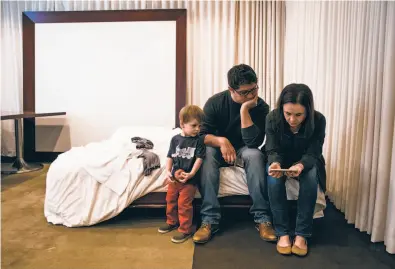  ?? Photos by Mason Trinca / Special to The Chronicle ?? Wine Country evacuees Luciano Tristan (center) and Julia Harkins watch Facebook Live video updates from the Sonoma County Sheriff ’s Office in a meeting room where the family is staying at the Clift hotel in S.F.