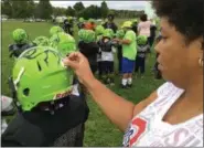  ?? RICHARD PAYERCHIN — THE MORNING JOURNAL ?? Leota Jordan, vice president of the board of the Lorain County Raging Raptors youth football team, attaches a commemorat­ive sticker to the helmet of a player at practice Oct. 2, at Gen. Johnnie Wilson Park in South Lorain.