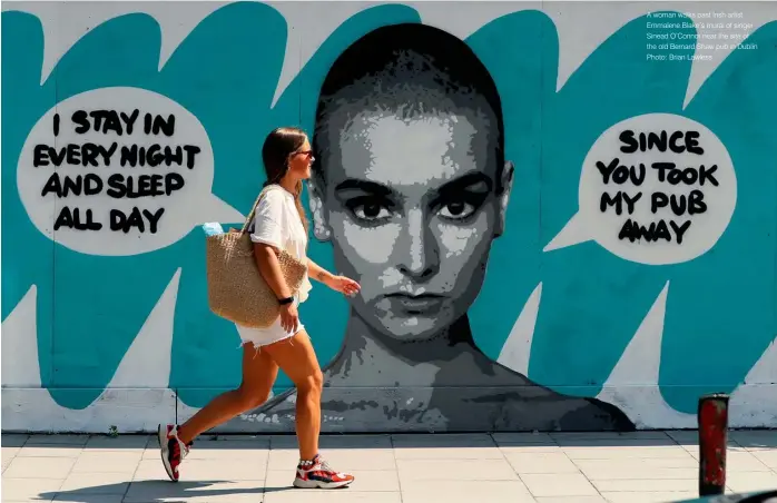  ?? Photo: Brian Lawless ?? A woman walks past Irish artist Emmalene Blake’s mural of singer Sinead O’Connor near the site of the old Bernard Shaw pub in Dublin