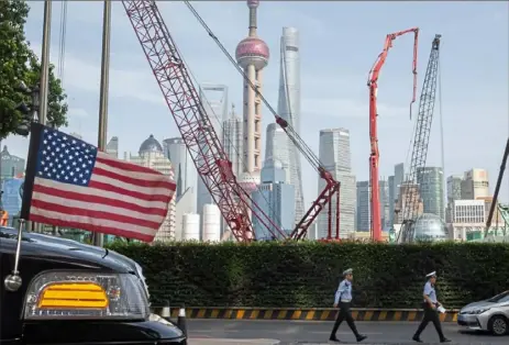  ?? Ng Han Guan/ Associated Press ?? Chinese traffic police officers walk by a U. S. flag on an embassy car outside a hotel in Shanghai on Tuesday. Two months after U. S.- Chinese talks broke down, President Donald Trump says he will impose new tariffs on Chinese products.