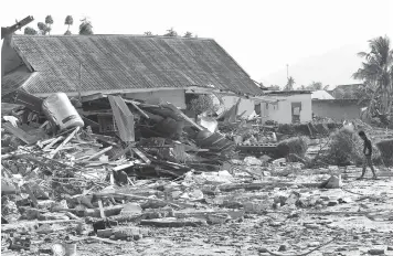  ?? Tatan Syuflana/Associated Press ?? ■ A man walks Monday by houses damaged in a massive earthquake and tsunami at Talise beach in Palu, Central Sulawesi, Indonesia.