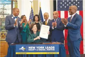  ?? DON POLLARD/OFFICE OF THE GOVERNOR VIA AP ?? New York Gov. Kathy Hochul, seated center, displays a bill Tuesday in New York to create a commission tasked with considerin­g reparation­s to address the persistent, harmful effects of slavery in the state. She is joined by, standing from left: James Sanders, N.Y. State Senator; Andrea Stewart-Cousins, Majority Leader of the N.Y. State Senate; Michaelle Solages, N.Y. State Assembly Woman; Rev. Al Sharpton; Carl Heastie, Speaker of the N.Y. State Assembly; Dr. Yohuru Williams, Founding Director of the Racial Justice Initiative at the University of St. Thomas.