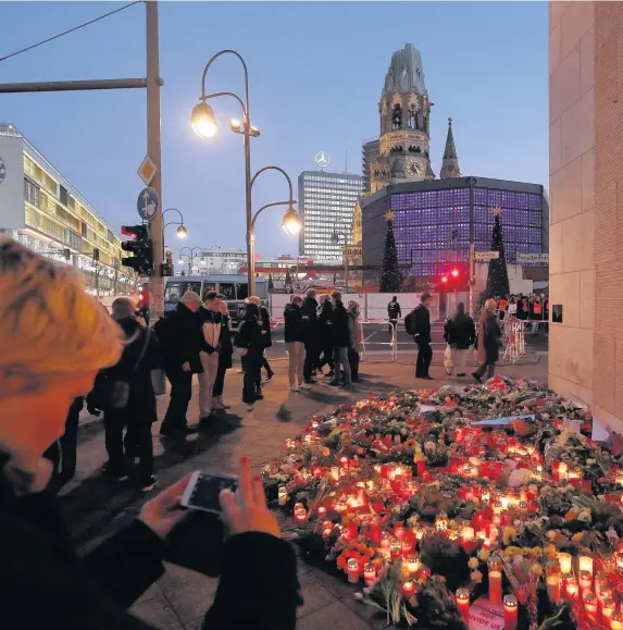  ?? Sean Gallup ?? > Mourners lay flowers and candles at a makeshift memorial near the site where a man drove a lorry into a Christmas market in Berlin, killing 12 people and injuring 48