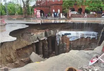  ?? AFP ?? Residents gather after a road caved in due to heavy rains. At least four people died of electric shocks while two others were killed after a building collapsed.