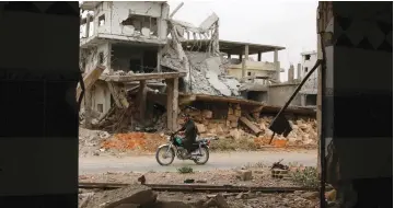  ?? (Reuters) ?? A MAN RIDES a motorcycle past damaged buildings in a rebel-held area of the southern Syrian city of Deraa yesterday.