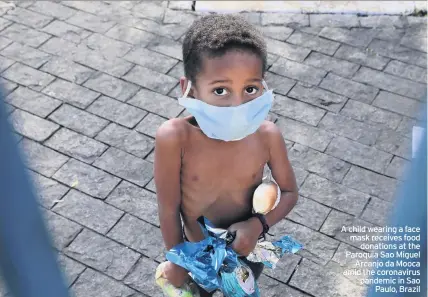  ??  ?? A child wearing a face mask receives food donations at the Paroquia Sao Miguel Arcanjo da Mooca amid the coronaviru­s pandemic in Sao Paulo, Brazil