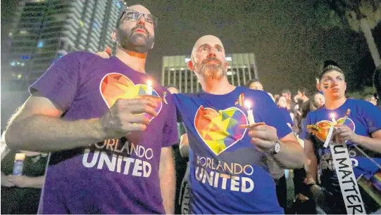  ?? JACOB LANGSTON/STAFF PHOTOGRAPH­ER ?? Seth Dobey, left, and Corey Alexander, center, hold candles Monday during a remembranc­e ceremony to honor the 49 Pulse shooting victims at Lake Eola Park.