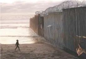  ?? AP FILE PHOTO/GREGORY BULL ?? A woman walks on the beach next to the border wall topped with razor wire in Tijuana, Mexico.