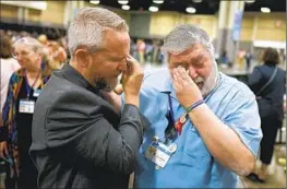  ?? Chris Carlson Associated Press ?? DAVID OLIVER, left, and David Meredith wipe away tears after the United Methodist Church General Conference voted to drop a ban on LGBTQ+ clergy.