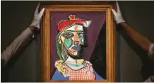  ??  ?? Gallery assistants hold an artwork by Spanish artist Pablo Picasso entitled ‘Femme au beret et a la robe quadrillee’ (Marie-Therese Walter) with an estimate price in the region of 35 million pounds, (50 million dollars), during a photocall at Sotheby’s...